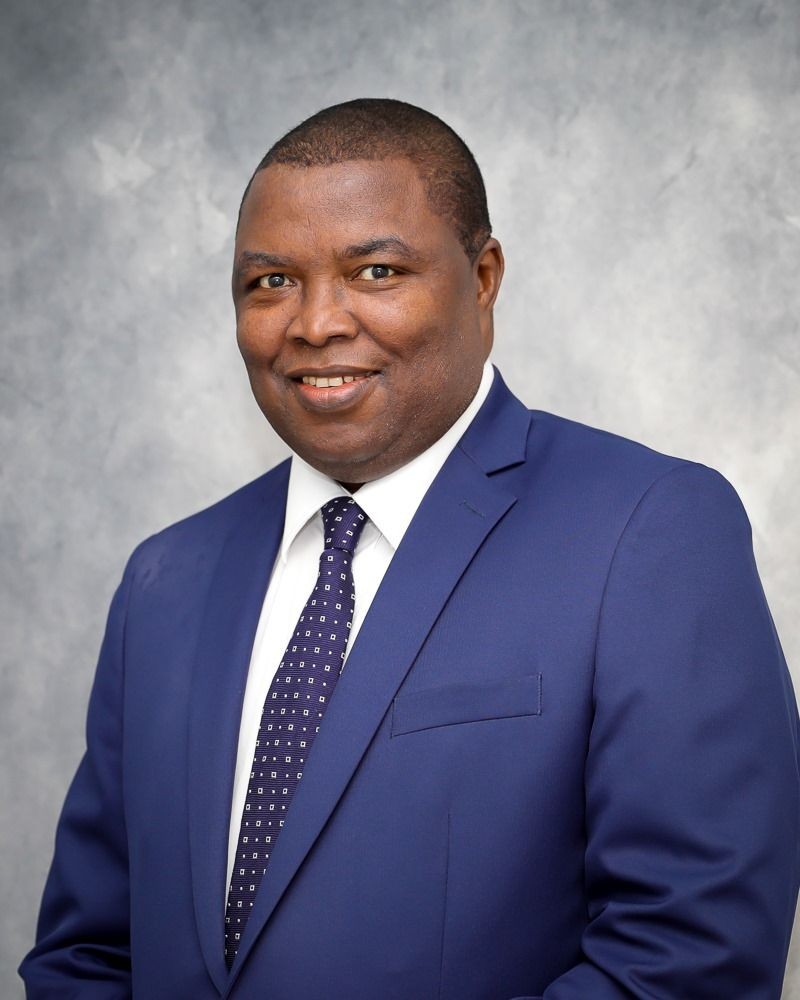 Man in blue suit and tie smiling against a gray background.